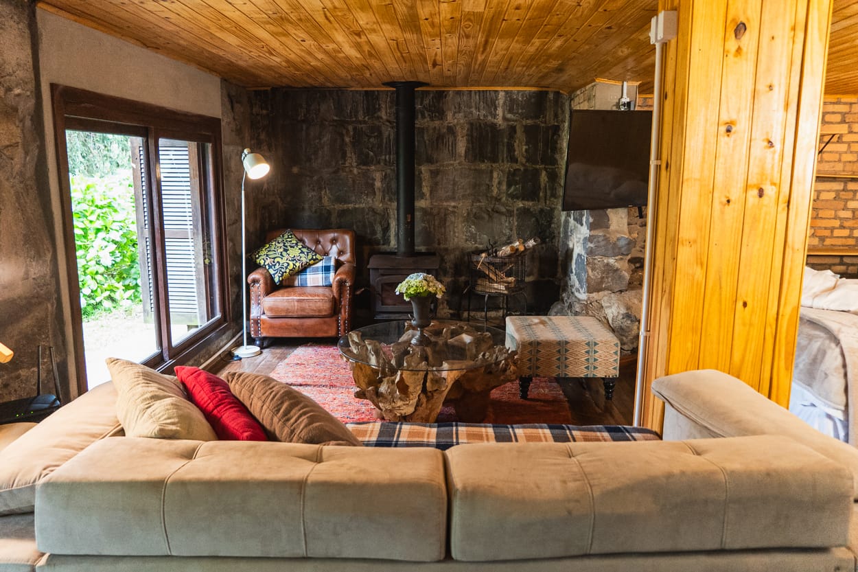 Sala do chalé com fogão a lenha e parede de pedra